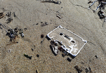 1980s plastic cassette tape frame on a sandy beach, highlighting ocean pollution. This stark image underscores the urgency of addressing marine debris.