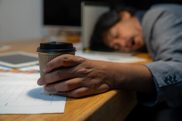 The man who worked hard fell asleep with a cup of coffee at the office.