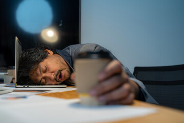 The man who worked hard fell asleep with a cup of coffee at the office.