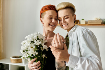 A lesbian couple with short hair standing together, each holding a colorful bouquet of flowers in...