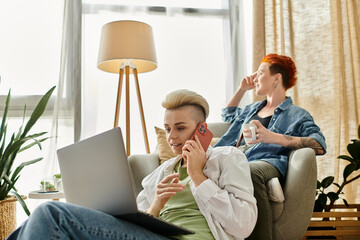 Two people, a lesbian couple with short hair, are sitting together in a chair, engaged in a deep conversation on the phone.
