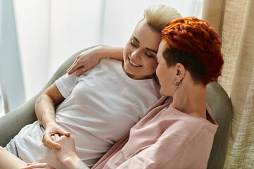 Two women with short hair embracing on a couch in a warm and loving gesture, exemplifying LGBTQ+...