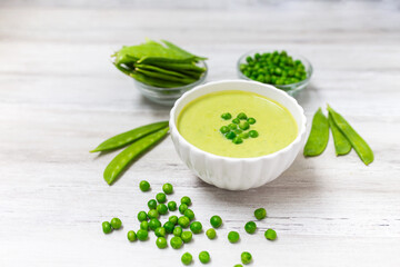 Cream soup with green pea on white wooden background.. 
