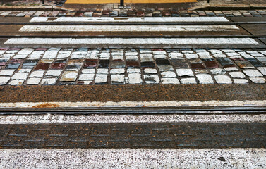 Pedestrian crossing over the tram tracks on a cobblestone pavement.