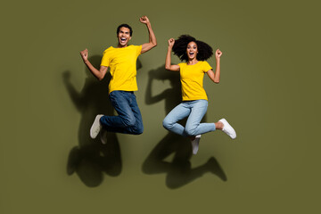 Full body portrait of two nice people raise fists jump wear t-shirt isolated on khaki color background