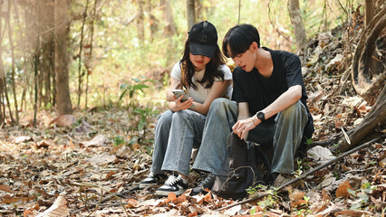 Young friends are sitting on the ground resting in the forest, Using a smartphone to explore routes...