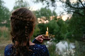 Girl with burning candle in candlestick outdoor, abstract natural background. rear view. religion,...