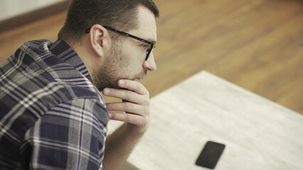 Sad bearded young man in casual sitting on couch at home. Phone on the table