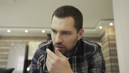 Thoughtful young bearded man sitting on sofa alone at home. Slow motion