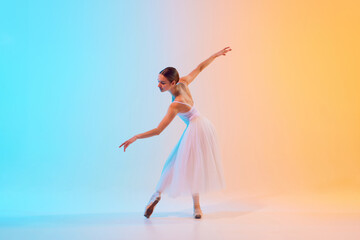 Grace in motion. Charming, young ballerina in classic ballet pose in neon light against blue-orange...