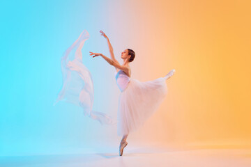 Fototapeta premium Talented young ballerina dancing in motion with fabric in neon light against blue-orange gradient background. Concept of art, movement, classical and modern fusion, beauty and fashion. Ad