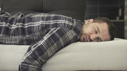 Young bearded man in casual clothes sleeping on the couch in a room at home