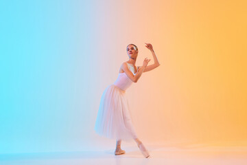 Elegant ballet performer in white tutu and pointe moves in dance in neon light against blue-orange...