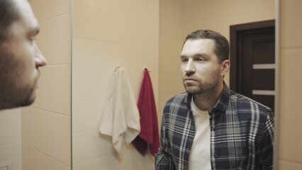 Handsome bearded young man looking in mirror in the bathroom. Slow motion