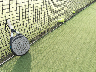 Closeup view of a paddle racket and balls in a padel tennis court near the net. Green background with white lines. Sport, health, youth and leisure concept. Sporty equipment. White lines in background