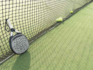Closeup view of a paddle racket and balls in a padel tennis court near the net. Green background...