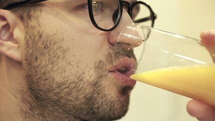 Young bearded guy in glasses drinking orange juice. Close up. Slow motion