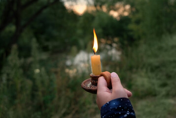 candlestick with burning candle in woman hand outdoor, abstract natural dark background. magic,...