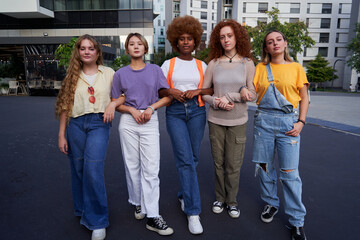 Multiethnic group of young women holding arm in arm looking at camera with seriousness. Concept of united female community, sorority, equality, feminism and empowerment.