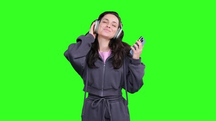 Woman enjoying music while using headphones and phone, dancing on the chroma key