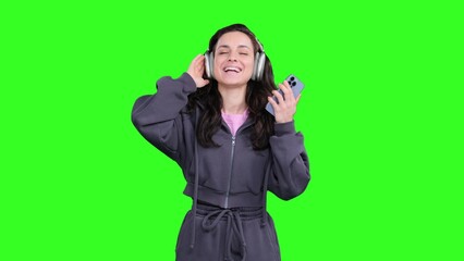 Smiling young lady listening the music with headphones on the chroma key