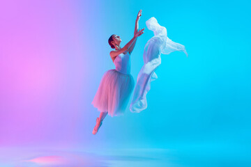 Light as silk. Graceful young ballet dancer performing with fabric in neon light against vivid...
