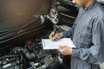 Auto check up and car service shop concept. Mechanic writing job checklist to clipboard to estimate...