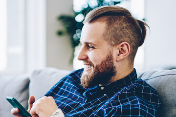 Cheerful hipster guy enjoying internet connection at home for chatting in social networks via...