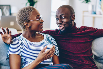 Positive african american couple in love sitting on comfortable couch having conversation about...