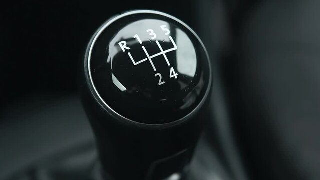 Black image of a car gear shift. The gear shift is black and white and has the numbers 1 through 5 on it.