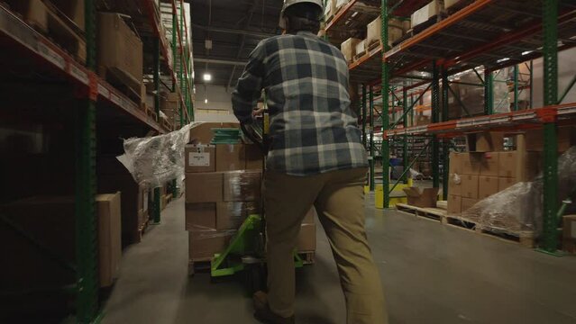 Tracking shot of worker in warehouse pushing merchandise with pallet jack / American Fork, Utah, United States