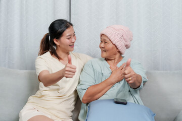 Young woman and elderly giving thumbs up, smiling at each. beanie, indicating cancer treatment....
