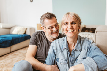 Joyful middle-aged couple laughing and smiling, enjoying quality time together at home, showcasing...