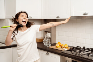Joyful Woman Singing In Kitchen Holding Utensil: Young adult enjoying life, spontaneous fun,...