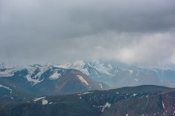 Dark atmospheric landscape with mountain silhouettes and large snow-capped peaked top in rainy low...
