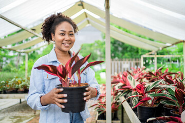 A woman is sitting in front of a plant nursery, smiling and holding a plant in her hand