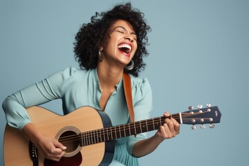Portrait of a joyful woman in her 30s playing the guitar in soft blue background