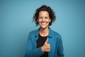 Portrait of a smiling woman in her 40s showing a thumb up in soft blue background