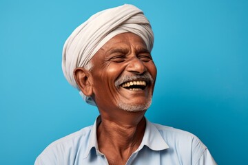 Portrait of a grinning indian man in his 50s laughing over soft blue background