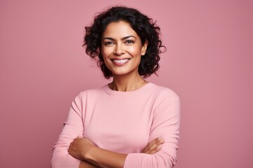 Fototapeta premium Portrait of a smiling indian woman in her 40s with arms crossed over soft pink background