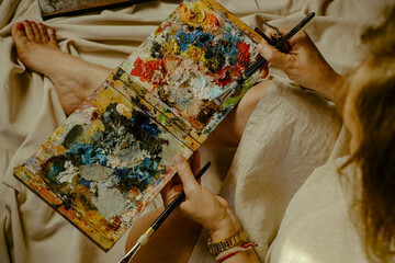 Palette with mixed paints holded by hands of woman artist, closeup. copy space for text.