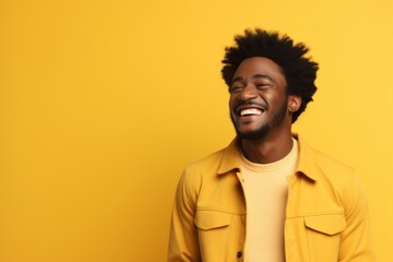 Portrait of a glad afro-american man in his 20s laughing isolated in soft yellow background
