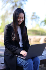 A Japanese businesswoman works on her laptop in the park, blending technology with outdoor comfort.