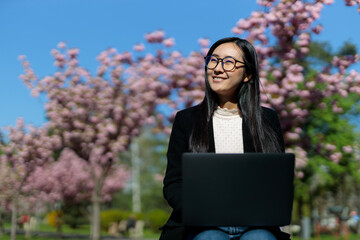 A Japanese woman enjoys working on her laptop in the park, combining education with outdoor...