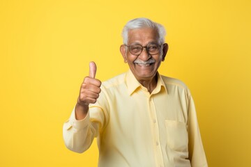 Portrait of a happy indian elderly man in his 90s showing a thumb up isolated on soft yellow background