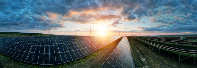 Photovoltaic power station and wind turbines at sunset panorama. Windmill turbines generating green...