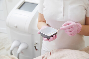 Cosmetologist applying gel before doing laser hair removal epilation on female leg in a salon