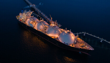 Aerial of Liquified Natural Gas LNG carrier moored to a small gas terminal at night. Fuel crisis....