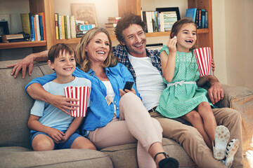 Obraz premium Happy family, relax and watching tv with popcorn on sofa for movie, weekend or holiday in living room at home. Mom, dad and children with smile and enjoying show, series or streaming service at house