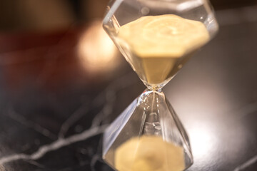 A sandglass or hourglass is placed on table. Interior decoration object photo, selective focus.